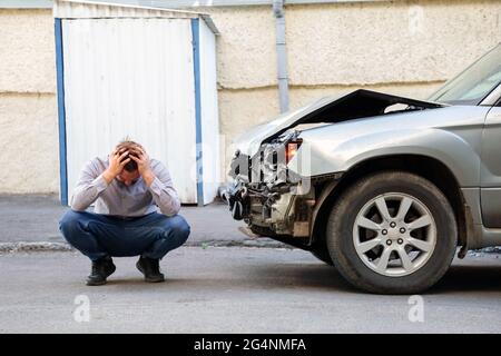 Jeune conducteur en voiture accident tenant sa tête près d'une voiture brisée sur la route après un accident de voiture. Homme caucasien visage tenant une blessure à la tête après Banque D'Images