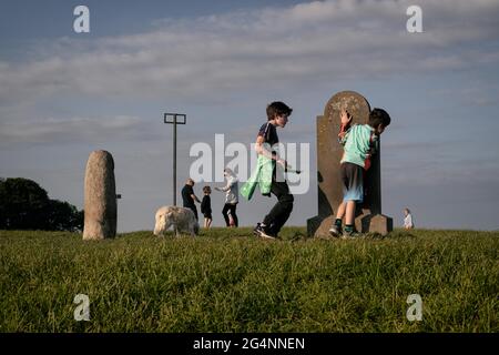 Colline de Tara, Irlande. 21 juin 2021. Les jeunes garçons jouent cacher et chercher et chasser autour de la pierre debout et du site de tombe au sommet de la colline de Tara.UN grand nombre de spectateurs, jeunes et vieux, beaucoup accompagnés de chiens, Se sont rassemblés sur la colline de Tara In Co. Meath pour admirer le coucher du soleil sur le solstice d'été du 21 juin. La colline de Tara est une tombe de passage néolithique et est un site d'importance historique ancienne dans le folklore irlandais. Crédit : SOPA Images Limited/Alamy Live News Banque D'Images