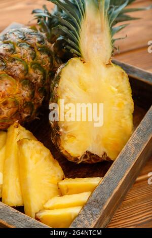 Ananas en tranches. Bromélain tropical fruit d'été ananas moitiés et ananas entier sur table brune sombre dans une boîte en bois. Banque D'Images