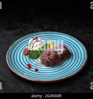 Fondant au chocolat servi sur une assiette bleue avec de la crème glacée et des baies sur une table sombre Banque D'Images