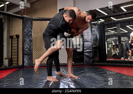 Les jeunes boxeurs de MMA combattants se battent dans des combats sans règles dans des octagons en anneau. Artistes martiaux mixtes pendant la lutte. Sport et boxe concept Banque D'Images