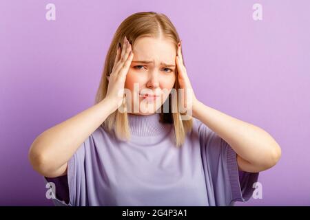 Femme éprouvant des maux de tête de stress tenant sa tête. Portrait émotionnel de la jeune femme triste. Émotions humaines de douleur et de regret sur la couleur isolée Banque D'Images