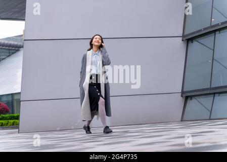 Vue en hauteur de la jeune femme d'affaires chinoise élégante tenant des appels téléphoniques mobiles et bavardant à l'extérieur du bâtiment de bureau moderne à Chengd Banque D'Images