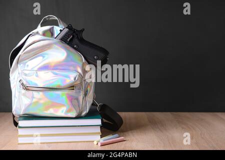 Pistolet et sac à dos avec livres sur table en classe. Concept de tir à l'école Banque D'Images