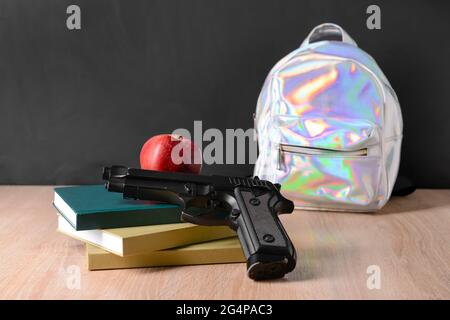 Pistolet avec livres et sac à dos sur table en classe. Concept de tir à l'école Banque D'Images