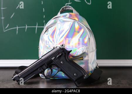 Pistolet et sac à dos sur table en classe. Concept de tir à l'école Banque D'Images