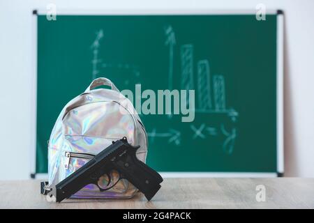 Pistolet et sac à dos sur table en classe. Concept de tir à l'école Banque D'Images