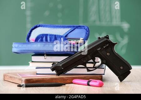 Pistolet et papeterie sur table en classe. Concept de tir à l'école Banque D'Images