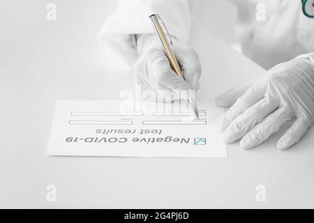 Médecin remplissant sous forme de résultat de test négatif Covid-19 en clinique, en gros plan Banque D'Images