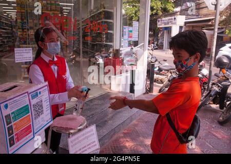 Lors d'une épidémie de COVID - 19, le gouvernement cambodgien impose un nouveau mandat de masque. Un adolescent de race mixte (cambodgien - américain), portant un masque facial/une couverture protectrice, se désinfecte les mains avant d'entrer dans une épicerie pendant la pandémie du coronavirus. Phnom Penh, Cambodge. 15 mars 2021. © Kraig Lieb Banque D'Images