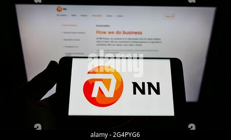 Personne tenant un téléphone portable avec le logo de la compagnie d'assurance néerlandaise NN Group N.V. à l'écran en face de la page Web d'affaires. Mise au point sur l'affichage du téléphone. Banque D'Images