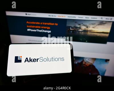 Personne tenant un téléphone portable avec le logo de la société norvégienne d'ingénierie Aker Solutions ASA sur l'écran en face de la page web. Mise au point sur l'affichage du téléphone. Banque D'Images