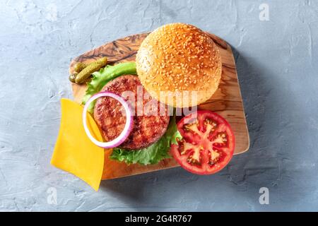 Ingrédients de Burger, tiré d'en haut sur un panneau de bois. Patty de bœuf, salade verte, cheddar, oignon rouge, tranche de tomate, et pains au sésame classiques Banque D'Images