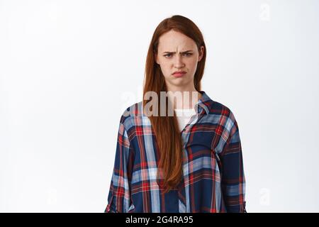 Portrait de la femme rouge grompie et en colère, regardez mal à la chose injuste, frognant et se portant, se tenant contrarié et offensé contre fond blanc Banque D'Images