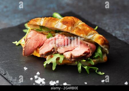 Sandwich croissant frais avec arugula et rôti de bœuf sur un tableau d'ardoise noir Banque D'Images