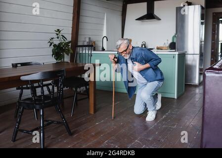 Homme malade avec béquille tenant la main sur la poitrine tout en tombant sur le sol Banque D'Images