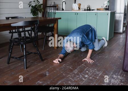 Homme âgé avec béquille tombant sur le sol dans la cuisine Banque D'Images