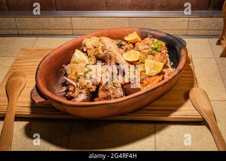 Poulet grillé maison aux épices coupées en morceaux dans un plat de cuisson en céramique rouge sur une planche de bois. Banque D'Images