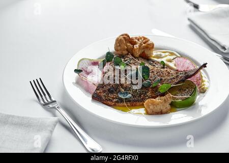 Poisson grillé avec légumes sur une assiette blanche, flet de poisson avec chou-fleur, radis et purée de pommes de terre, gros plan. Banque D'Images