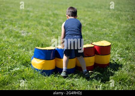 L'enfant surmonte un parcours d'obstacle. Jeux pour enfants en été. Reste du garçon dans l'air frais. L'enfant joue sur l'herbe verte. Sport doux Banque D'Images