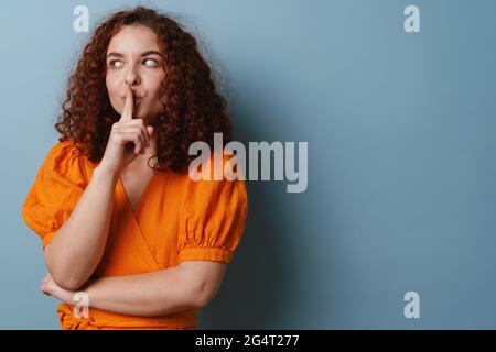 Heureux redhead maully fille montrant le geste de silence isolé sur fond bleu Banque D'Images