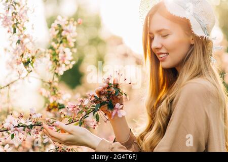 Belle jeune femme de printemps dans un chapeau, dans des fleurs roses parfumées dans un parc de fleurs d'été, femme dans un jardin de fleurs, sur un chaud jour de printemps ensoleillé, t Banque D'Images