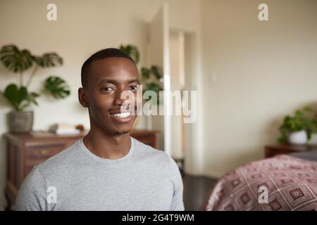 Jeune Africain assis dans sa chambre et souriant Banque D'Images