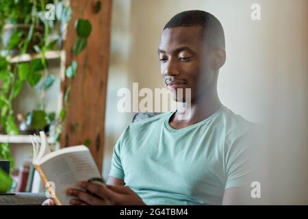 Un jeune homme africain lisant un livre sur son canapé Banque D'Images