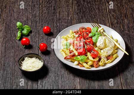 Pâtes au caprese italien au four composé de penne, de bacon, de tomates cerises et de mozzarella, nappées de parmesan râpé et de basilic frais servi sur une assiette Banque D'Images