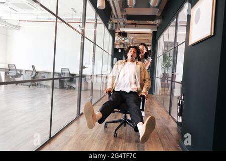 Jeune couple s'amusant comme une femme pousse l'homme le long de la passerelle du bureau ouvert moderne dans la chaise Banque D'Images