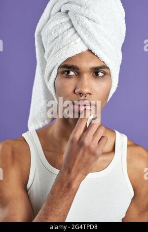 Transgenre jeune homme appliquer les lèvres balsam dans le portrait de serviette. Modèle Afroamerican utiliser le baume rouge à lèvres Banque D'Images