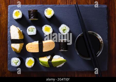 Maki végétarien et sushis nigiri faits maison sur une assiette d'ardoise avec un bol de sauce soja et des baguettes Banque D'Images