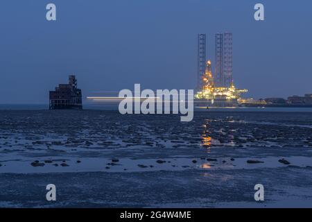 Lumières floues d'un navire se déplaçant derrière le fort de grain dans le Swale avec l'engin de forage amarré à Sheerness en arrière-plan pris la nuit. Banque D'Images