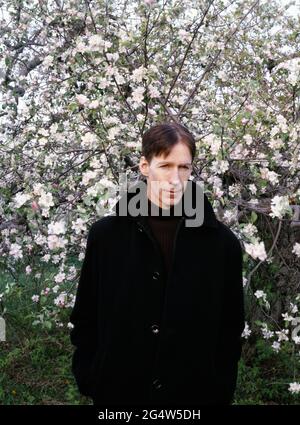 Un jeune modèle masculin portant une couche de finition dans un verger de pommes de la Nouvelle-Angleterre au printemps Banque D'Images