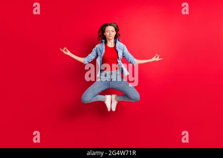 Photo de la taille du corps pleine longueur d'une fille gaie sautant vers le haut pratiquant le yoga asana méditant l'arrière-plan rouge vif isolé Banque D'Images