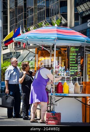 Hot Dog Stand centre-ville de Toronto : une vendeuse de rue vendant de la nourriture et des boissons au bord de la route avec son chariot placé sous un parapluie coloré, un homme et un W Banque D'Images