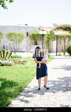 Maman porte une petite fille le long du chemin dans le parc Banque D'Images