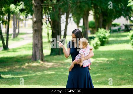 Maman porte une petite fille dans ses bras et la montre dans la distance avec sa main Banque D'Images