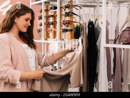 Vue latérale d'une femme souriante et de grande taille qui fait du shopping dans un petit magasin de vêtements Banque D'Images