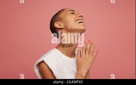 femme à tête rasée souriant sur fond rose. Femme androgyne avec exprimer vous-même écrit sur le cou. Banque D'Images