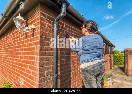 Femme fixant des éclairages extérieurs sur un mur externe. Banque D'Images