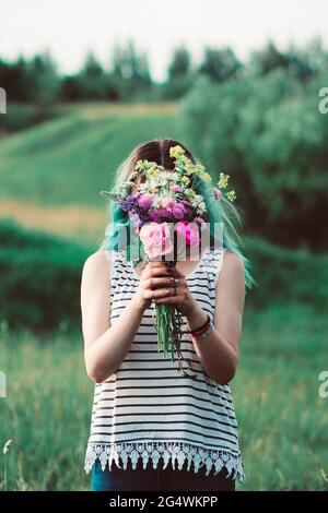 fille couvrant son visage derrière un bouquet de fleurs fraîchement cueillies Banque D'Images