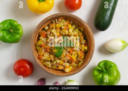 Légumes colorés dans un bol en céramique avec une branche de persil et d'ingrédients. Concept de cuisine espagnole. Pisto manchego. Vue de dessus. Banque D'Images