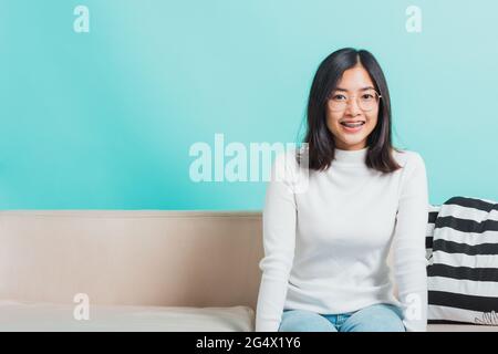 Asiatique belle jeune femme portant des lunettes de vue assis sur un canapé regardant l'appareil photo, la relaxation portrait de la femme heureuse souriant dans la vie en studio est prise de vue Banque D'Images