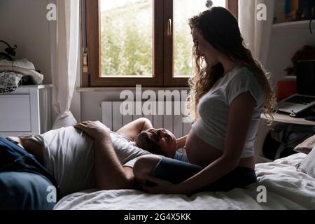 Femme enceinte assise par un homme allongé sur le lit dans la chambre Banque D'Images