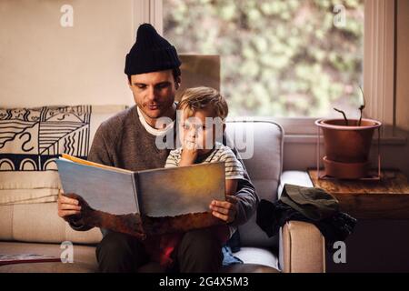 Père lisant l'histoire à son fils tout en étant assis sur le canapé à la maison Banque D'Images