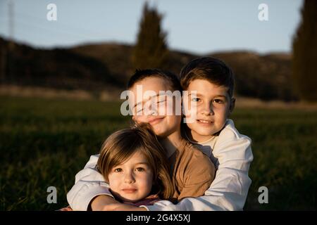 Frère et soeur assis avec les bras autour au champ agricole Banque D'Images