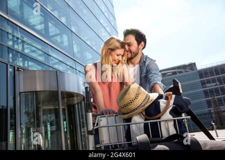 Happy young couple avec chariot à bagages à l'extérieur du terminal de l'aéroport Banque D'Images