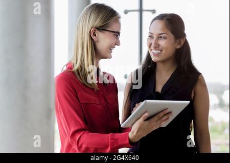 Femmes d'affaires souriantes discutant sur tablette numérique au bureau Banque D'Images