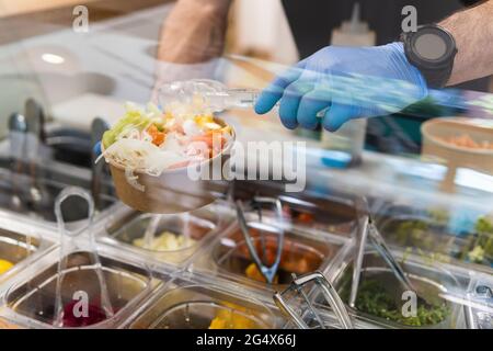 Chef avec des gants de protection pour préparer la salade au bar du restaurant Banque D'Images
